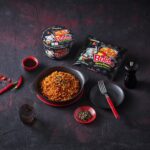 Samyang Buldak Original spicy ramen packet and cup noodle with a prepared bowl of stir-fried noodles
